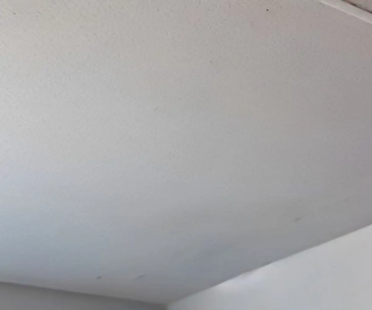 A close-up view of a drywall ceiling with a noticeable bulge or 'pillowing' defect.